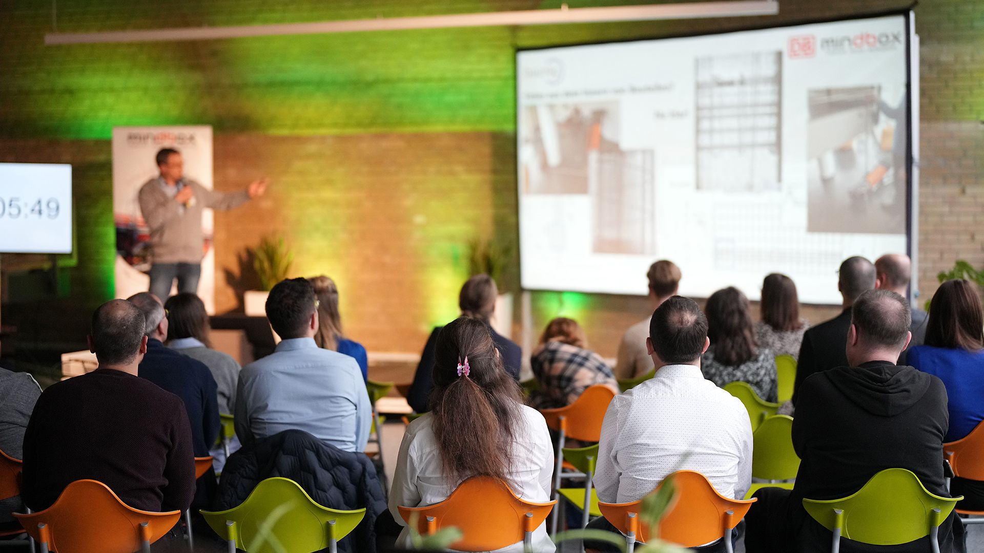 Several people are seated in a meeting room, listening to a presentation.