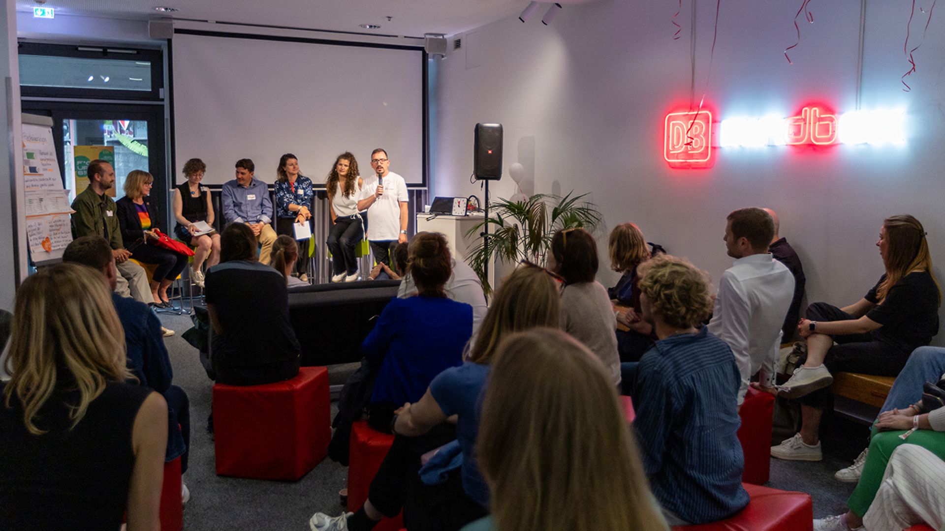 Several people are sitting on a stage and speaking to an audience.