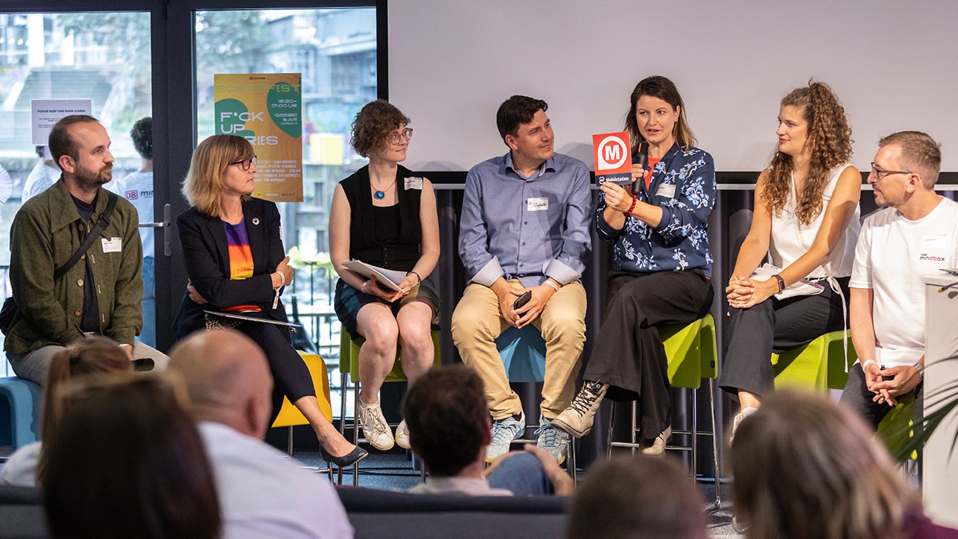 Several people are sitting on a stage and speaking to an audience.