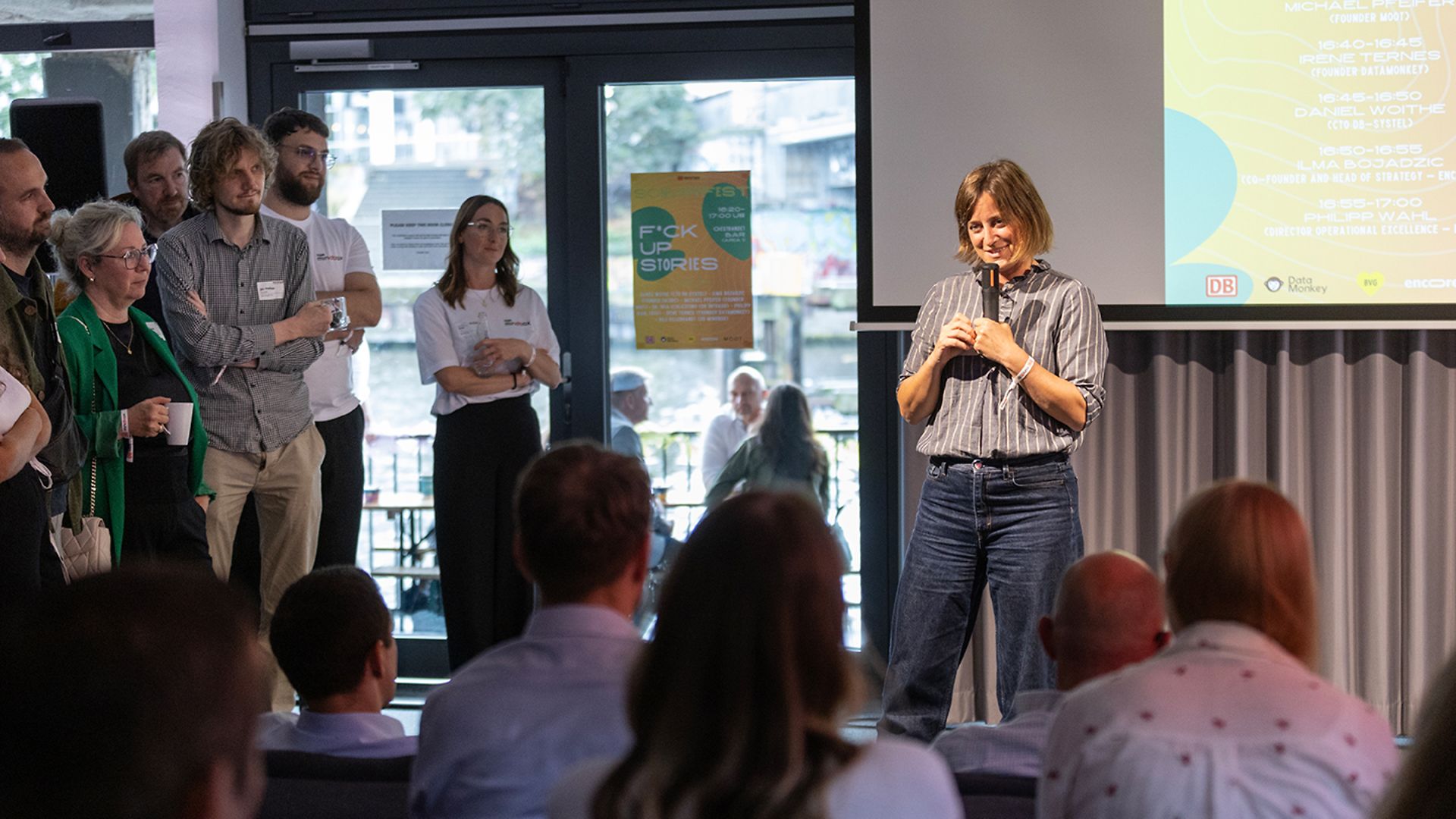 A woman is standing on a stage and speaking to an audience.