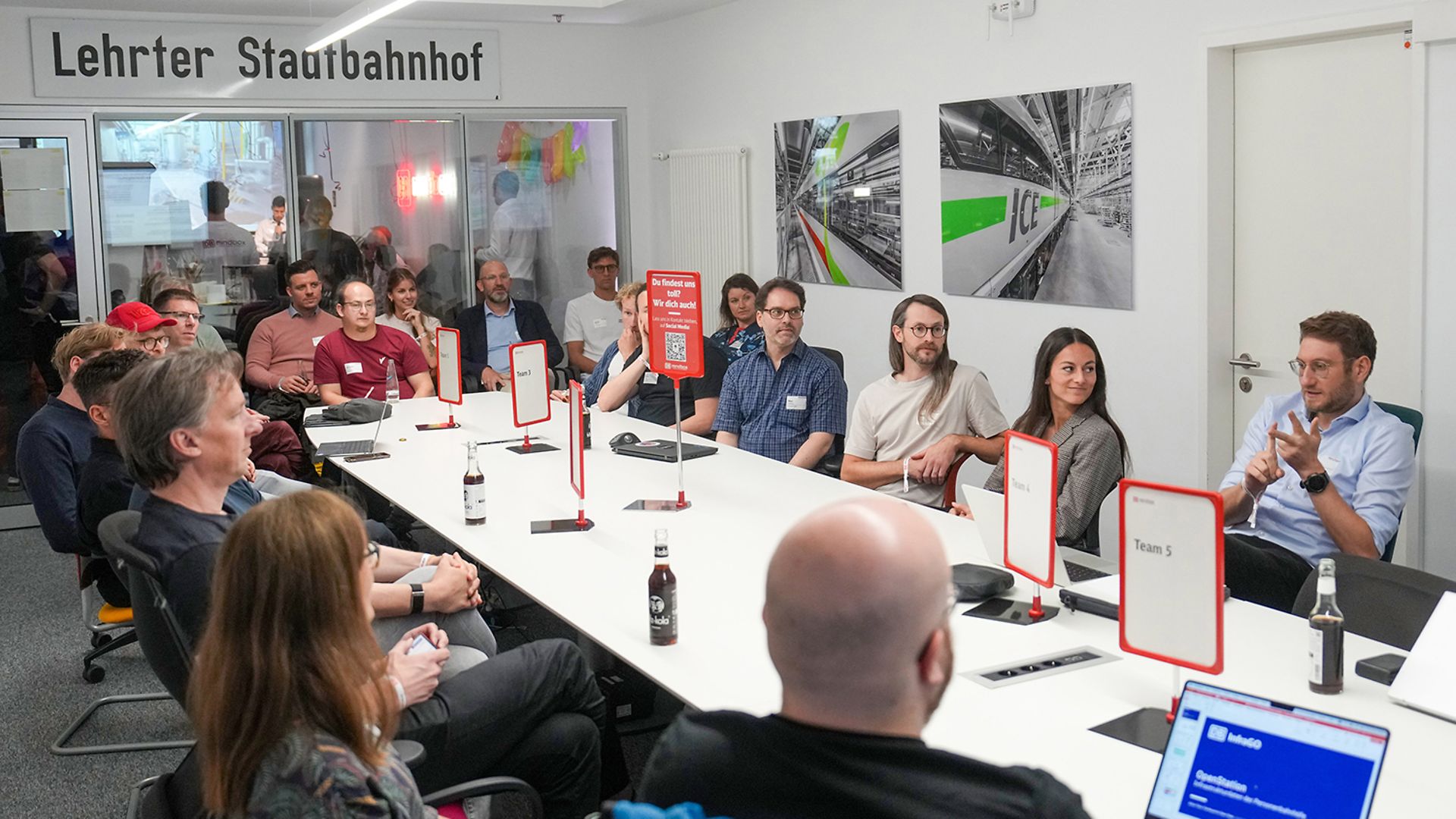 Several people are seated in a meeting room, listening to a presentation.